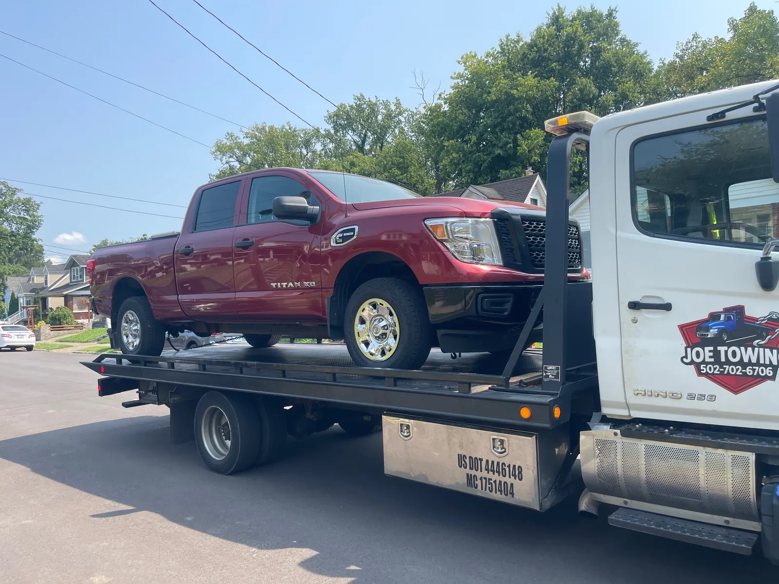 Joe Towing flatbed carrying a red pickup, the company logo and number on the truck door.